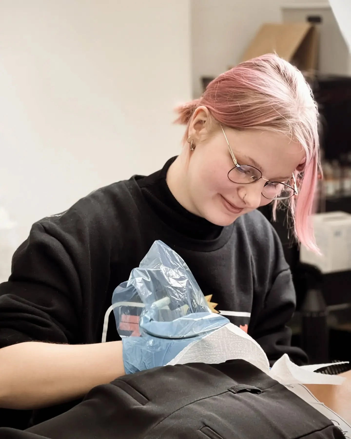Klara Keczyńska w okularach i czarnej bluzie pracuje nad tatuażem przy stanowisku.