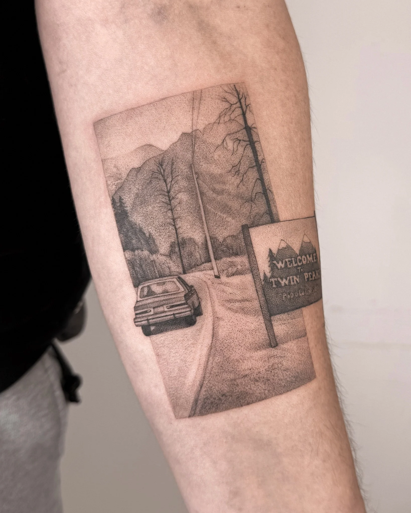 Tatuaż przedstawiający drogę prowadzącą przez górski krajobraz, samochód oraz znak „Welcome to Twin Peaks” na ramieniu., zdjęcie 2 z 2