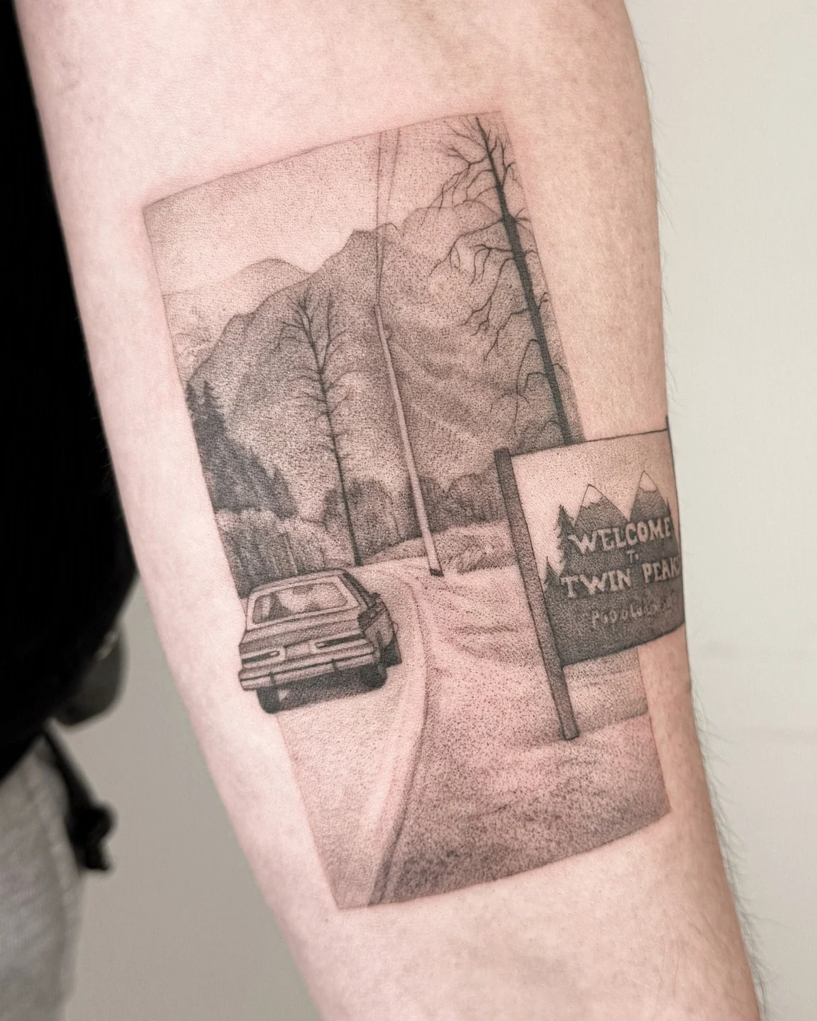 Tatuaż przedstawiający drogę prowadzącą przez górski krajobraz, samochód oraz znak „Welcome to Twin Peaks” na ramieniu., zdjęcie 1 z 2