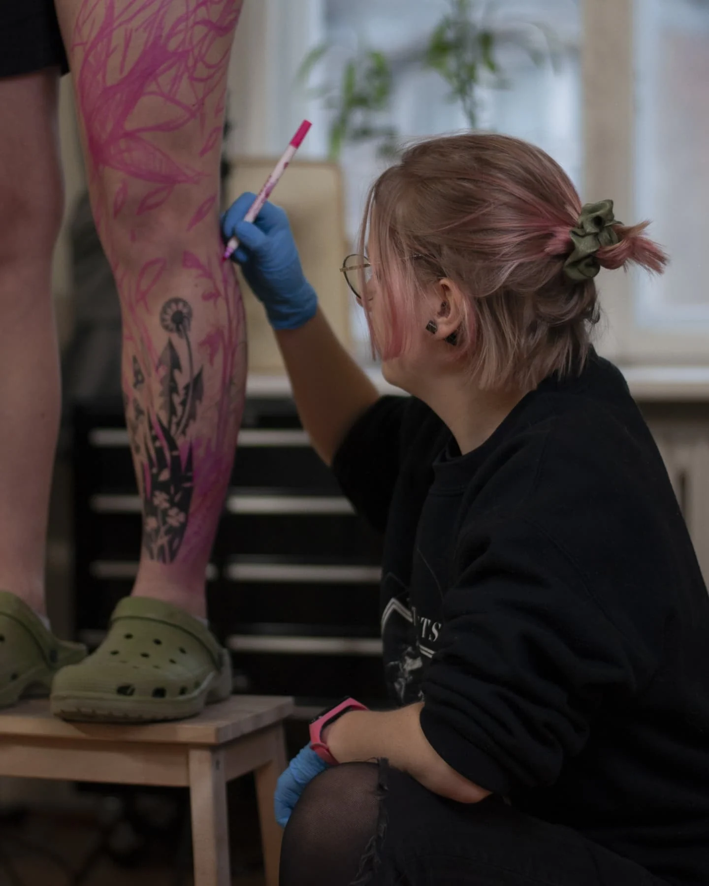 Klara Keczyńska podczas pracy nad kwiatowym tatuażem na nodze; na skórze widoczny jest czarny fragment wzoru oraz różowy zarys projektu.