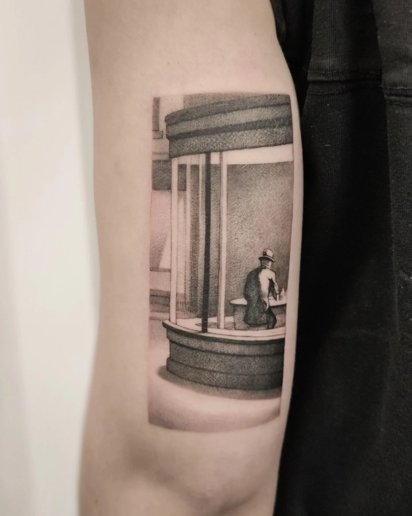 Tatuaż przedstawiający osobę siedzącą przy oknie lub witrynie, wykonany w monochromatycznej tonacji na podstawie obrazu Edwarda Hoppera., zdjęcie 3 z 3