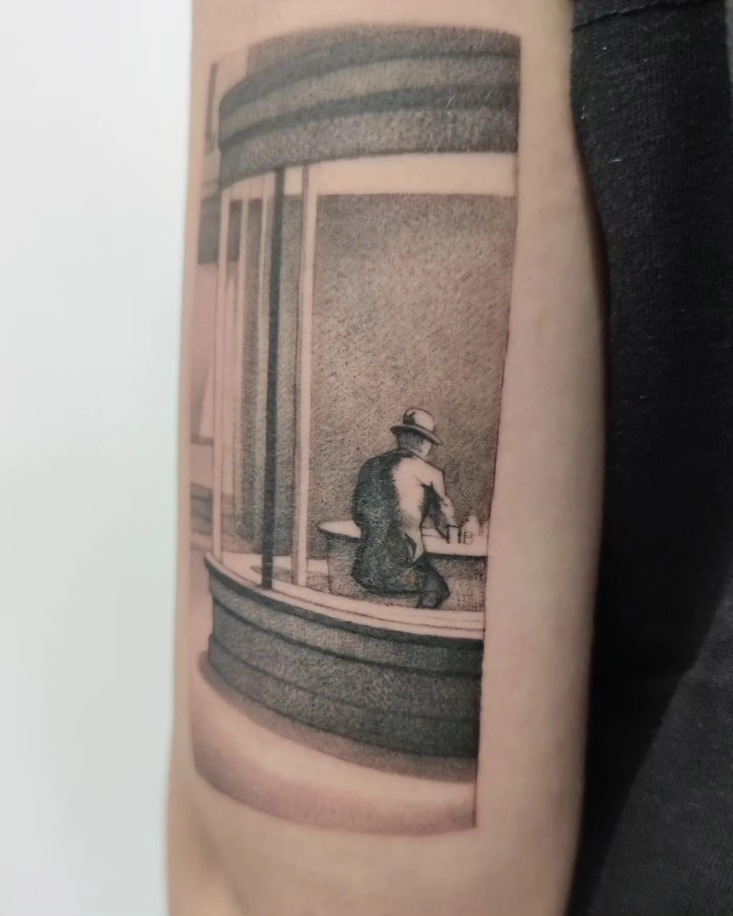 Tatuaż przedstawiający osobę siedzącą przy oknie lub witrynie, wykonany w monochromatycznej tonacji na podstawie obrazu Edwarda Hoppera., zdjęcie 2 z 3