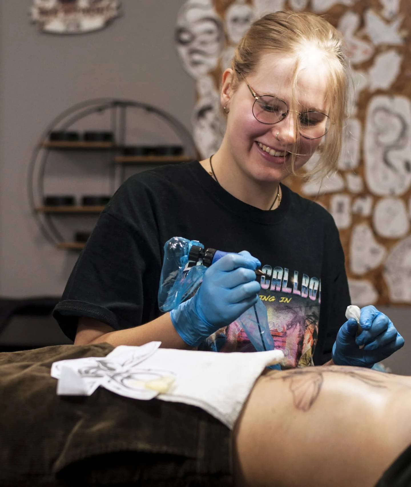 Klara Keczyńska w rękawiczkach tatuuje klienta w studiu, trzymając maszynkę do tatuażu.