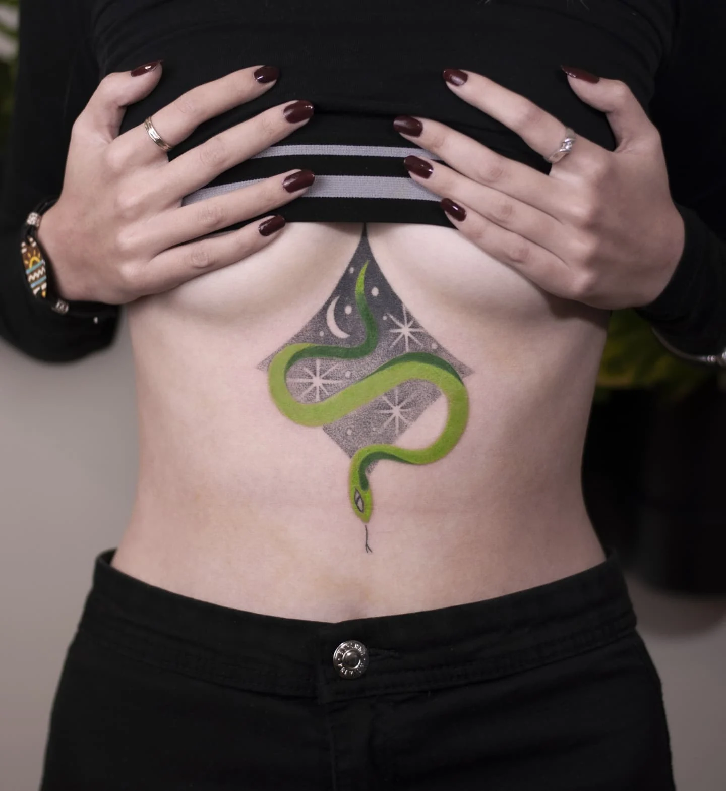 Kolorowy zielony wąż wśród jasnych, gwiaździstych motywów na skórze modelki; widoczny tatuaż cover up na środku tułowia.