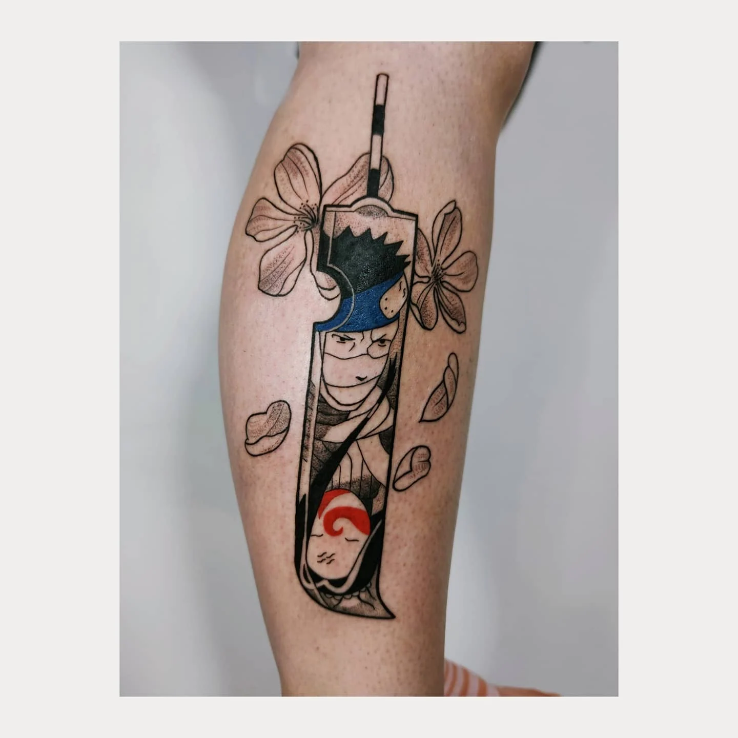 Pionowy tatuaż przedstawiający Zabuzę i Haku z anime Naruto, otoczonych kwiatami i liśćmi; widoczne są czarne kontury oraz niebieskie i czerwone akcenty.