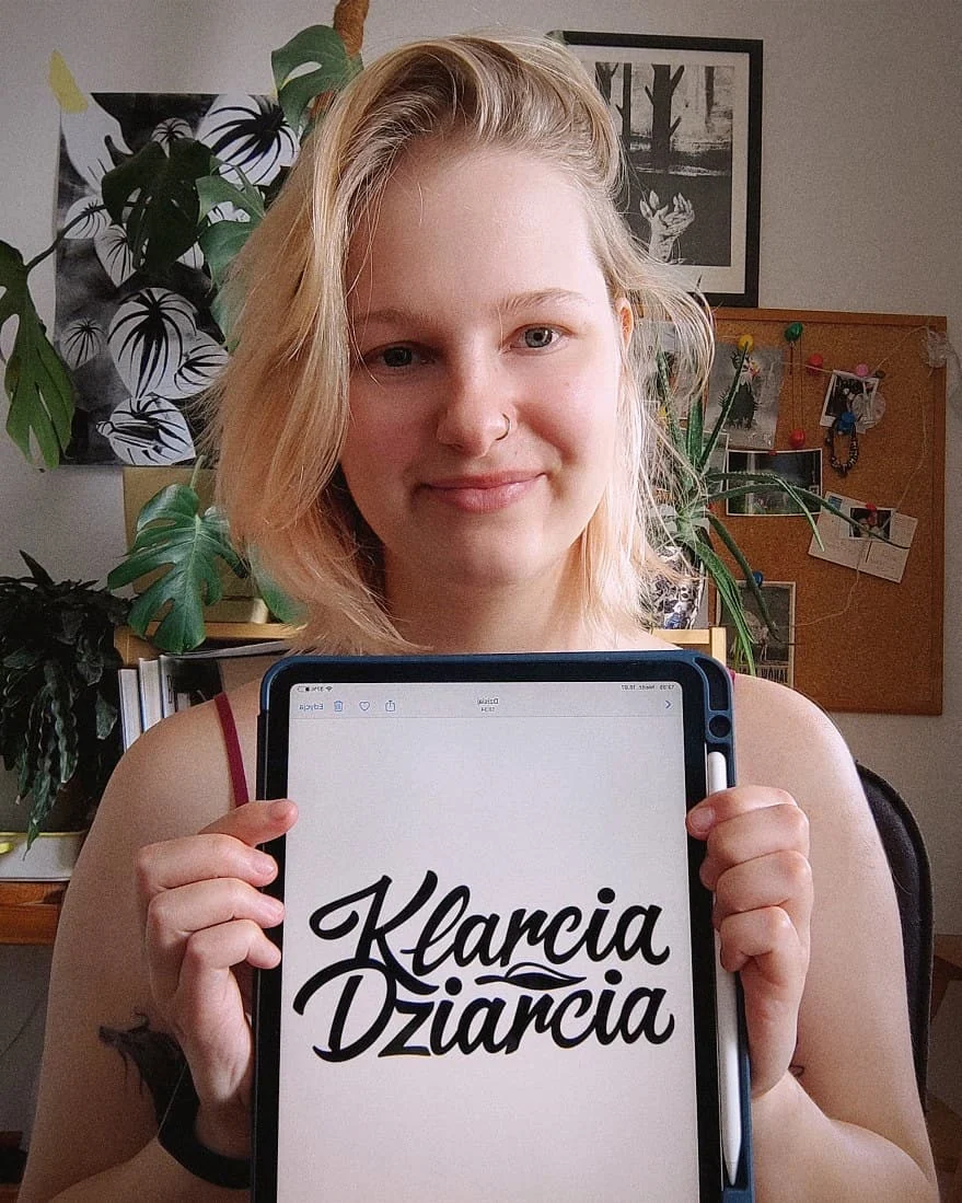 Klara Keczyńska trzyma tablet z wyświetlonym logo „Klarcia Dziarcia”.