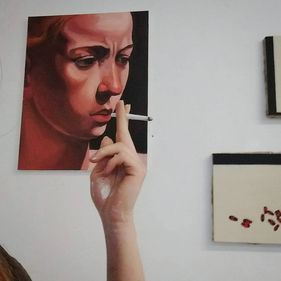 Portret kobiety z papierosem prezentowany na ścianie podczas wernisażu; obok widoczne są fragmenty innych prac.