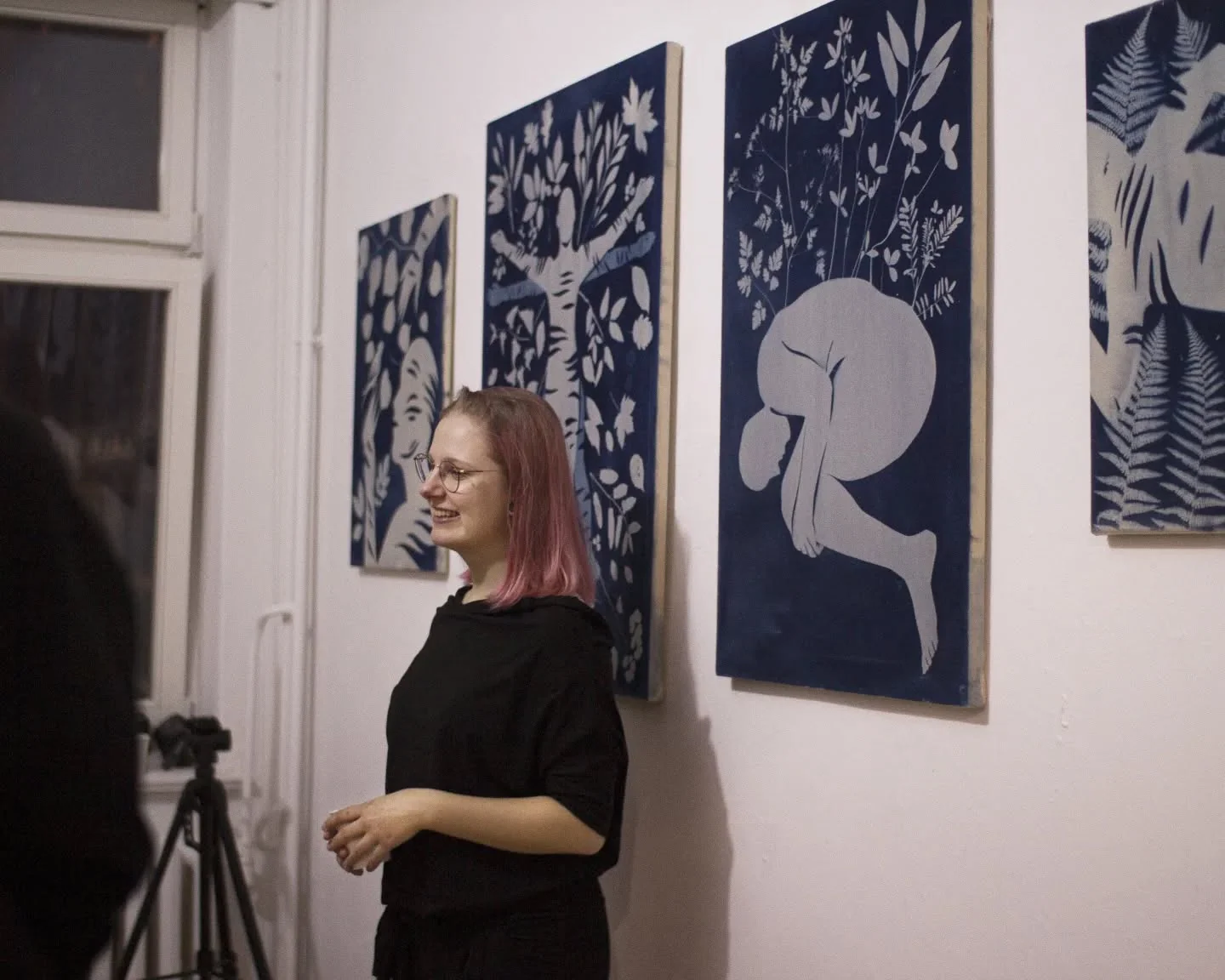 Dokumentacja wystawy dyplomowej: osoby na czarnej, rozsypanej ziemi, z widocznymi botanicznymi tatuażami; w tle na ścianie zawieszono wycięte liście., zdjęcie 6 z 10