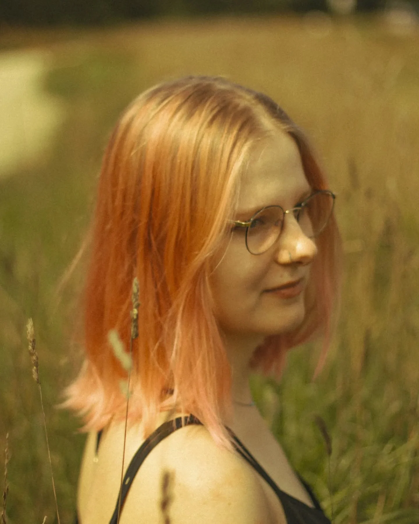 Portret Klary Keczyńskiej w okularach i czarnej sukience, stojącej wśród wysokich traw; na ramionach widoczne są tatuaże., zdjęcie 4 z 4
