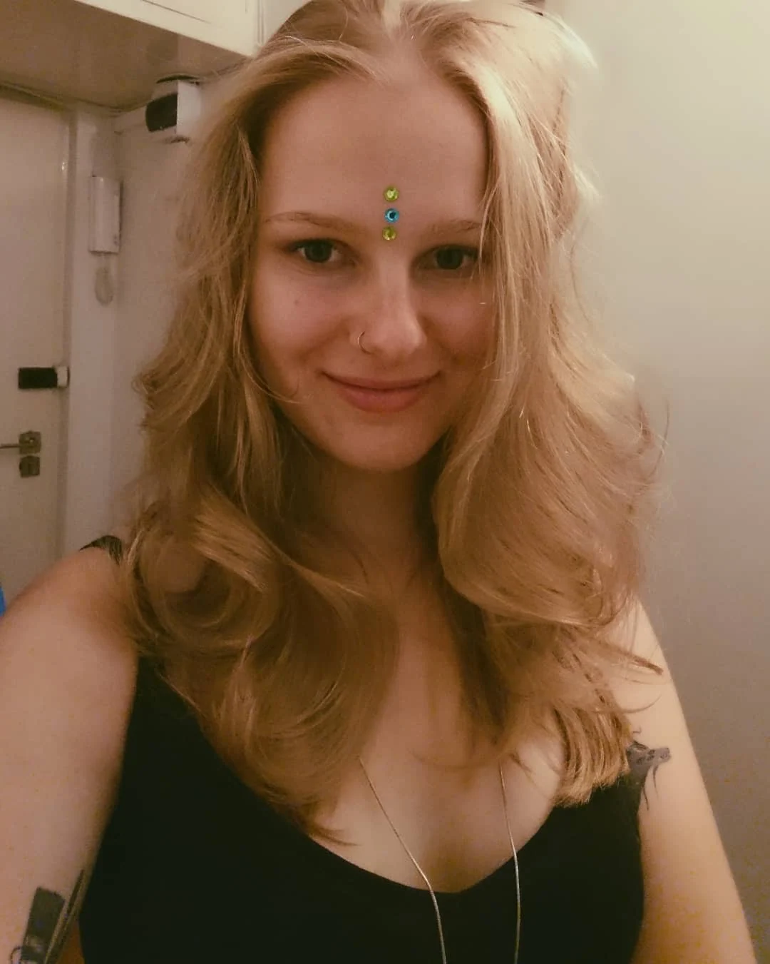 Portret Klary Keczyńskiej z rozpuszczonymi blond włosami, w czarnej bluzce i z ozdobą między brwiami.