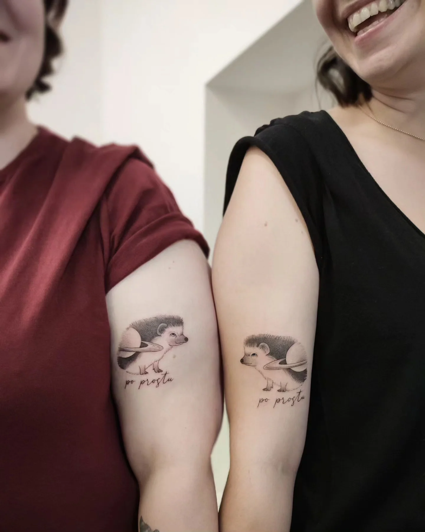 Dwa dopasowane czarno-szare tatuaże przedstawiające jeże z motywem Saturna i napisem „po prostu”, pokazane na ramionach dwóch osób oraz na zbliżeniach., zdjęcie 4 z 6