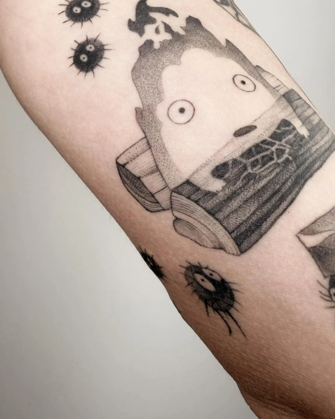 Wygojony tatuaż na ramieniu przedstawiający Calcifera oraz małe czarne kurzyki inspirowane filmami Studia Ghibli., zdjęcie 2 z 4