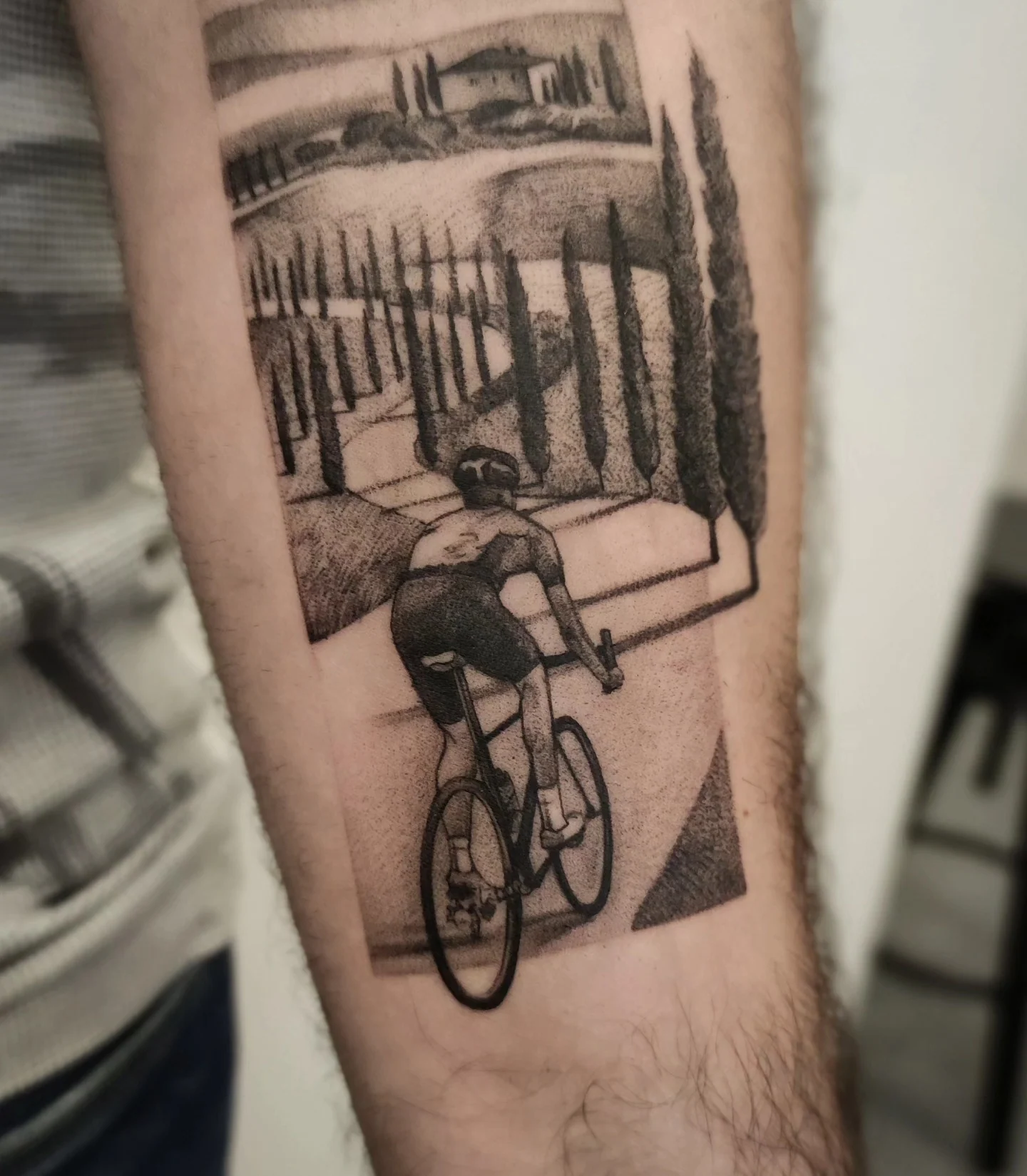 Tatuaż przedstawiający rowerzystę jadącego przez krajobraz z cyprysami, wzgórzami i drogą, wykonany na przedramieniu., zdjęcie 3 z 3