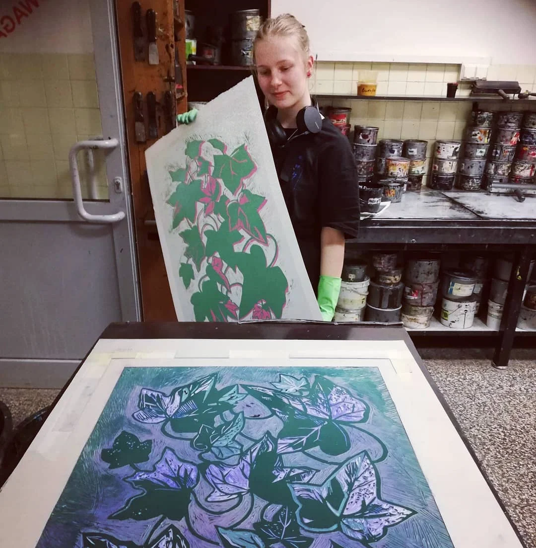 Klara Keczyńska prezentuje botaniczną ilustrację linorytem w pracowni; na stole widać odbitkę z motywami roślinnymi.
