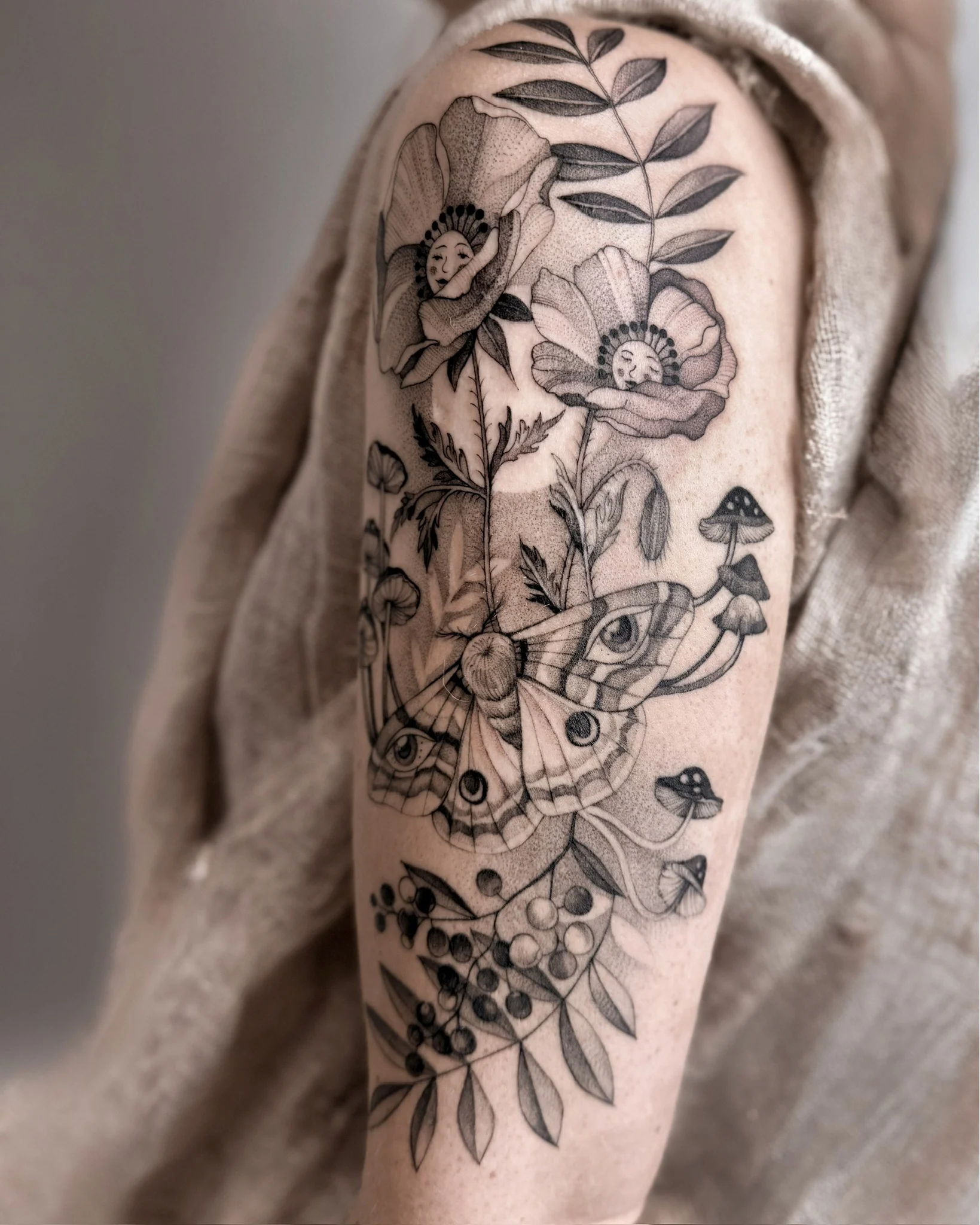 Botaniczna kompozycja tatuażu na ramieniu, przedstawiająca kwiaty maku, śpiące laleczki, ćmę, grzyby i gałązkę jarzębiny., zdjęcie 1 z 3