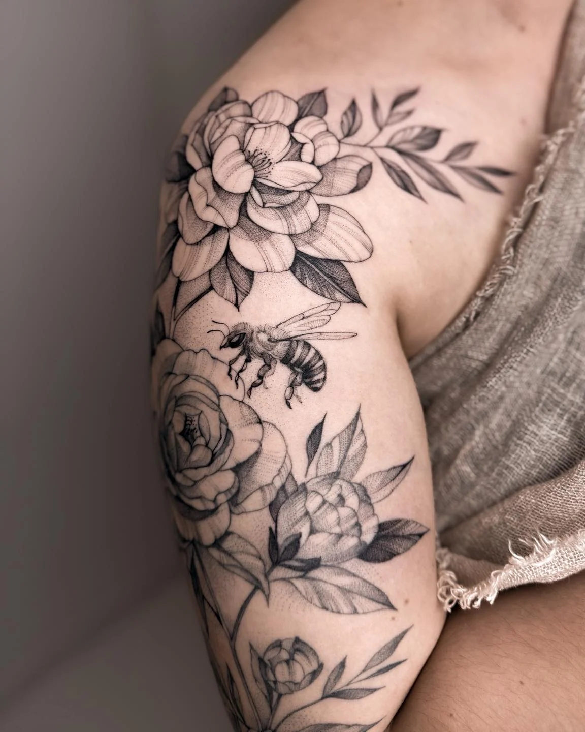 Botaniczna kompozycja tatuażu na ramieniu, przedstawiająca kwiaty i pszczołę; na zdjęciach widoczny jest także ciemny chrabąszcz., zdjęcie 1 z 7