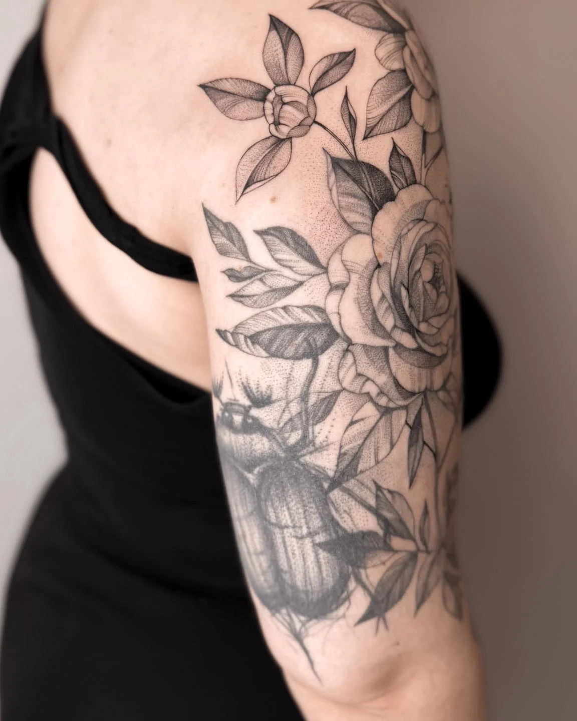 Botaniczna kompozycja tatuażu na ramieniu, przedstawiająca kwiaty i pszczołę; na zdjęciach widoczny jest także ciemny chrabąszcz., zdjęcie 5 z 7