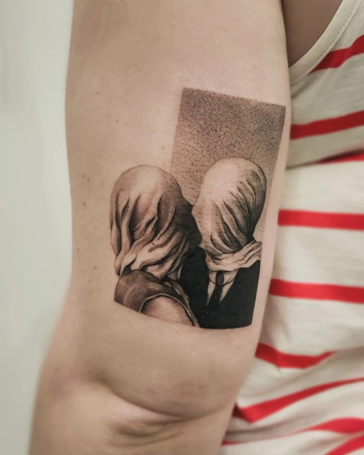 Zbliżenia tatuażu przedstawiającego dwie postacie z zasłoniętymi twarzami, inspirowanego obrazem „Kochankowie” René Magritte’a., zdjęcie 1 z 4