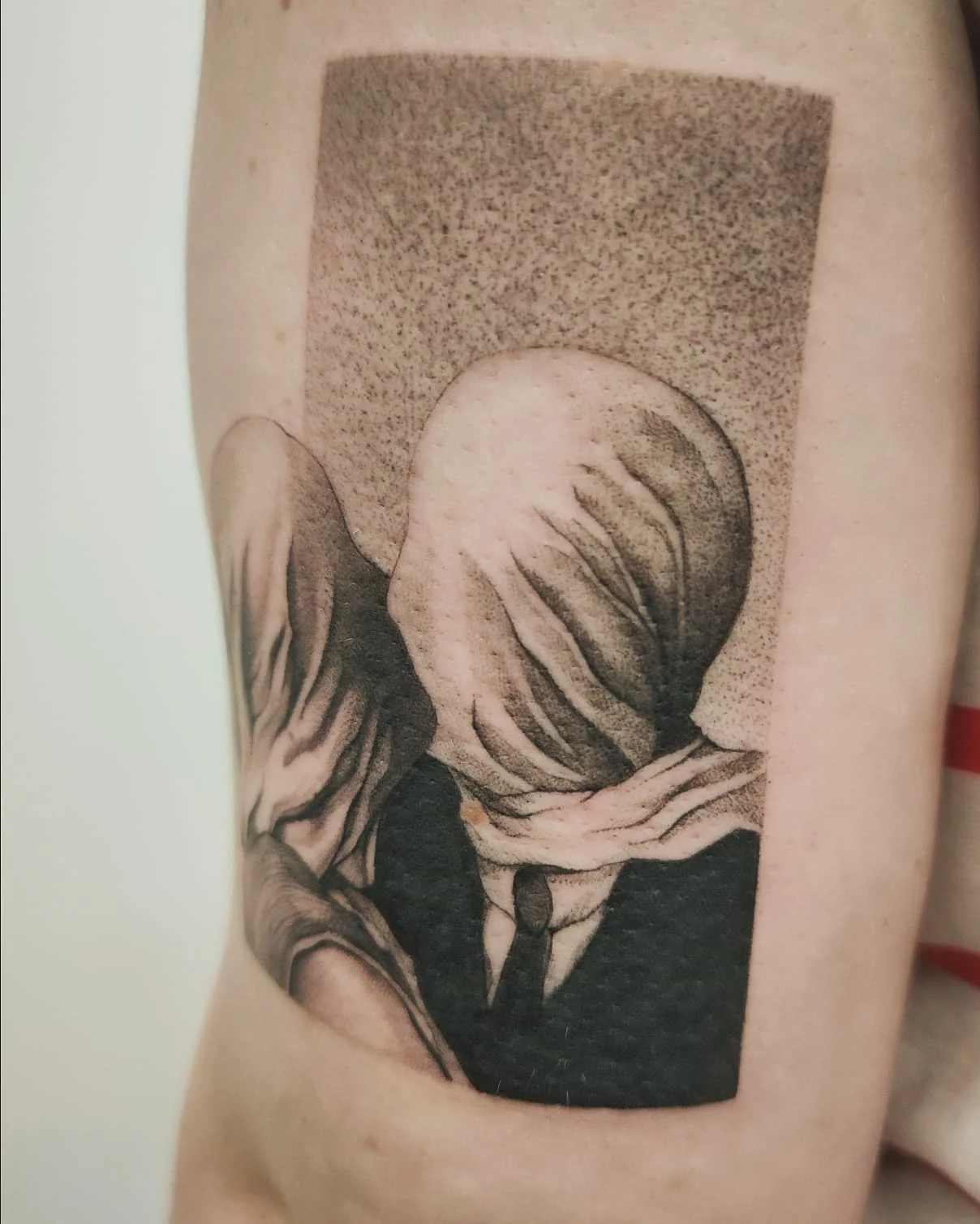 Zbliżenia tatuażu przedstawiającego dwie postacie z zasłoniętymi twarzami, inspirowanego obrazem „Kochankowie” René Magritte’a., zdjęcie 2 z 4