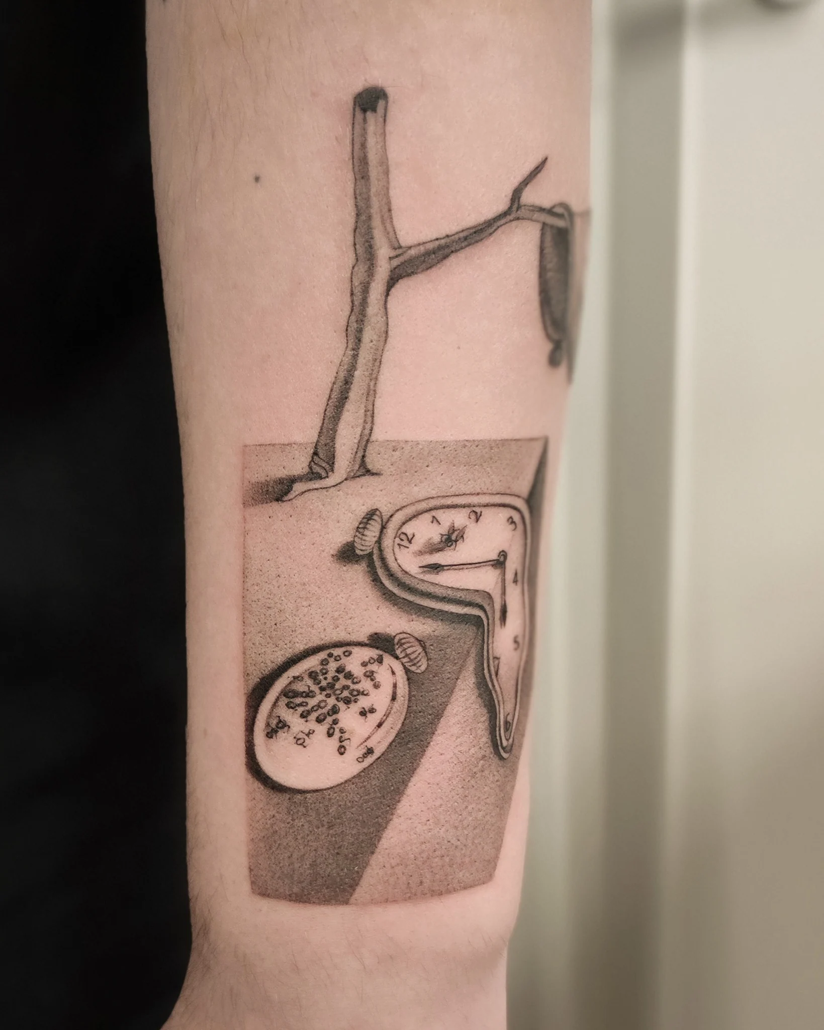 Tatuaż przedstawiający miękkie, rozpływające się zegary oraz surrealistyczną scenę inspirowaną obrazem „Trwałość pamięci” Salvadora Dalego., zdjęcie 2 z 3